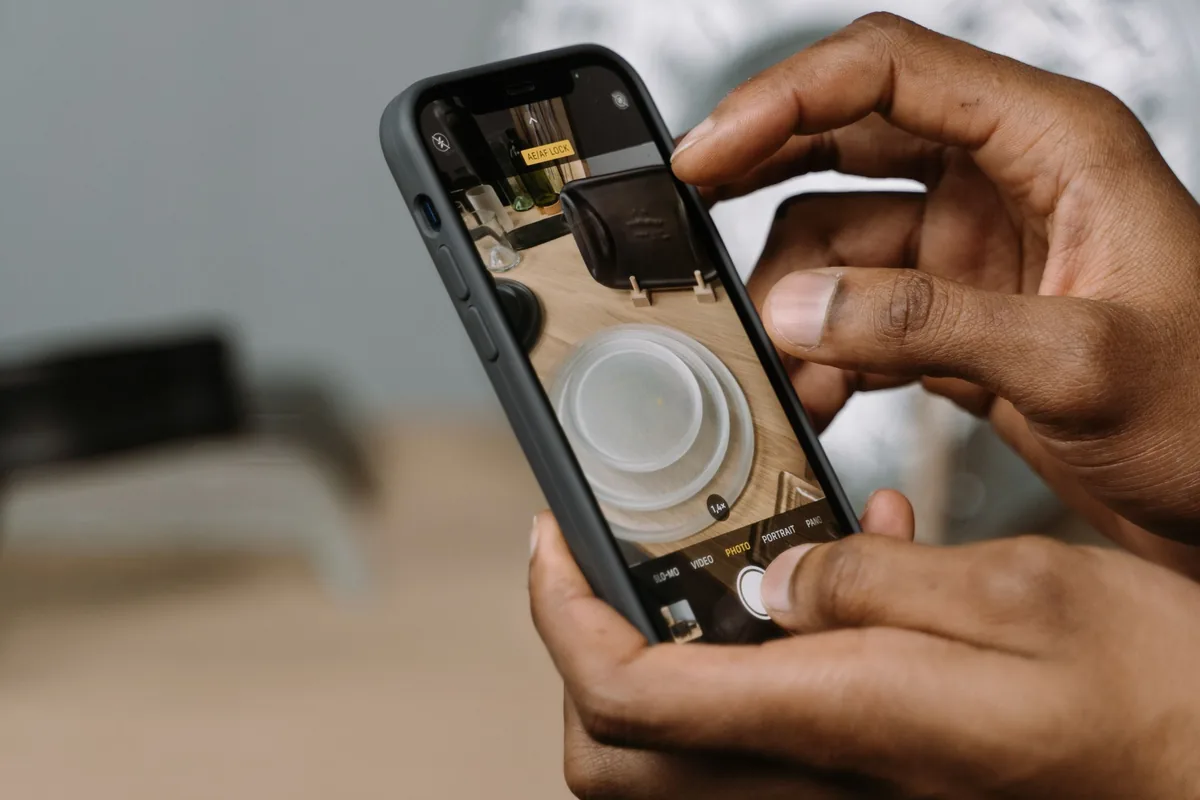 H&auml;nde halten ein Smartphone mit ge&ouml;ffneter Kamera-App &uuml;ber einem Tisch