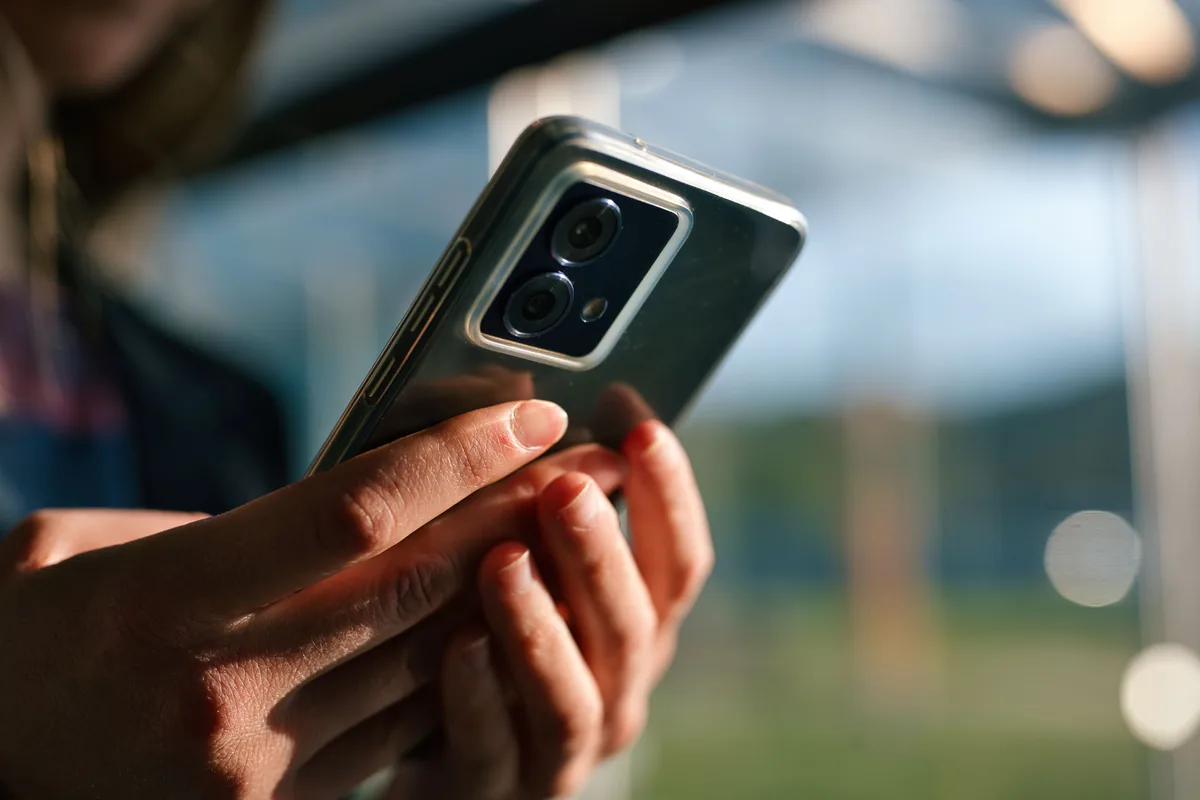 Nahaufnahme von H&auml;nden, die im Freien ein Smartphone halten