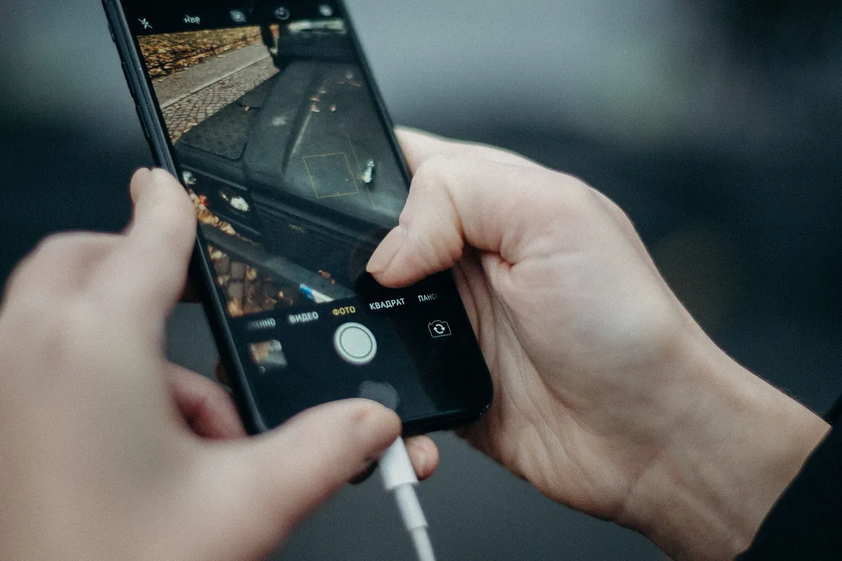 H&auml;nde halten ein Smartphone, an dessen Unterseite ein wei&szlig;es Ladekabel steckt